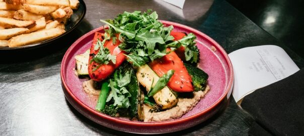 Grilled vegetable plate with red peppers, zucchini, asparagus, and fresh greens served on a purple plate at a Denver restaurant