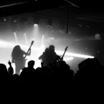 Crowd enjoying a live rock concert at a Denver music venue with silhouetted guitarists and bright stage lights.
