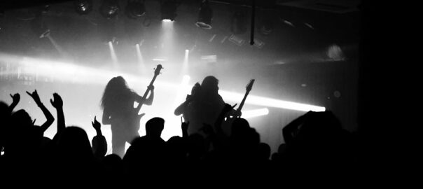 Crowd enjoying a live rock concert at a Denver music venue with silhouetted guitarists and bright stage lights.